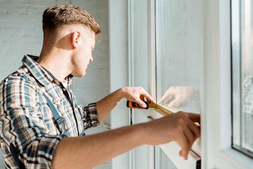 Person measuring the inside of a window frame with a measuring tape.