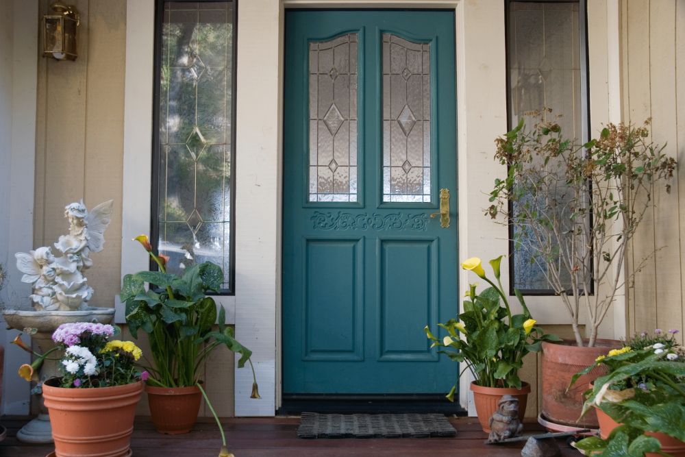 Teal door with yellow and pink flowers and plants in pots in the entry way.