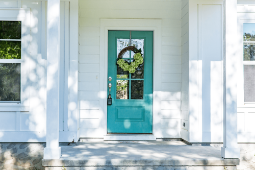 Teal front door with white cladding surrounding house exterior.